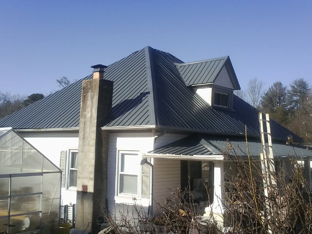 Dark blue standing seam metal roof on a white farmhouse with dormer — Slate & Tile Roof Repair by Roofing Brothers in Genoa