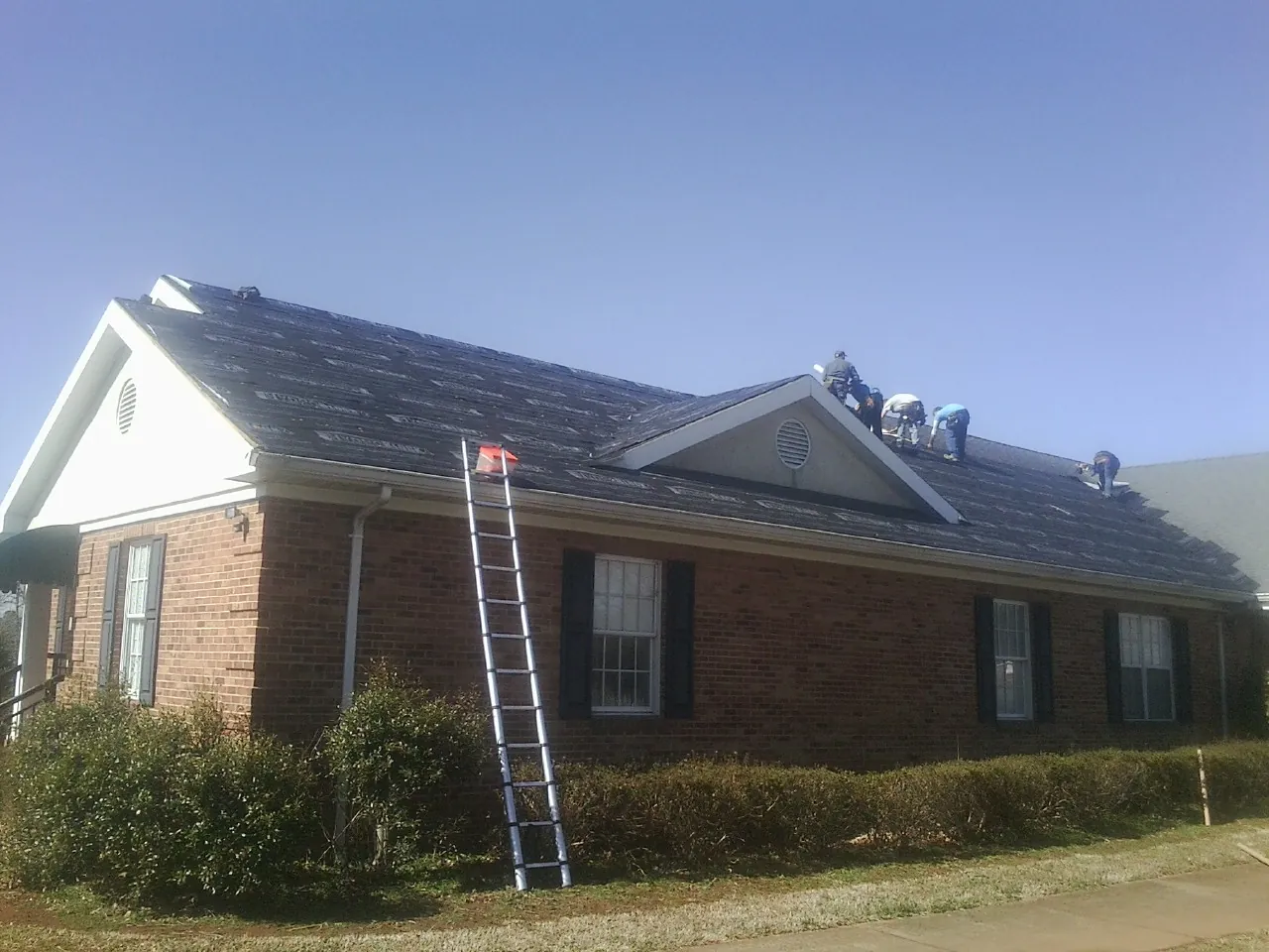 Crew tearing shingles off a brick ranch roof with a ladder set — Emergency Roof Repair work by our crew in Genoa