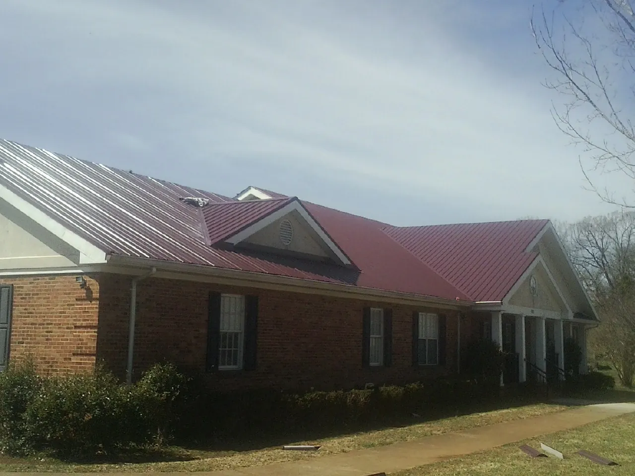 Red metal roof with gabled entries on a long brick building, from a Hail Damage Roof Repair job in Genoa