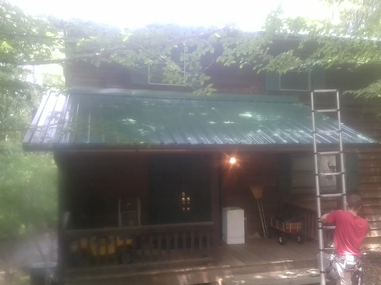 Worker on a ladder at the green porch roof of a wooded cabin in Genoa