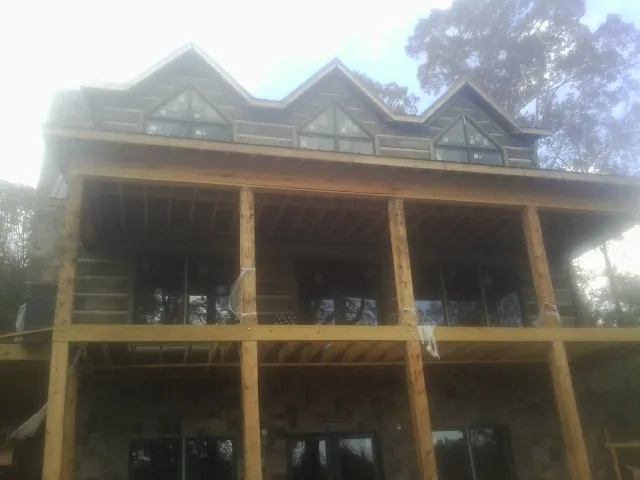 Dormers and porch framing on a large log home under construction — Roof Coating work by our crew in Genoa