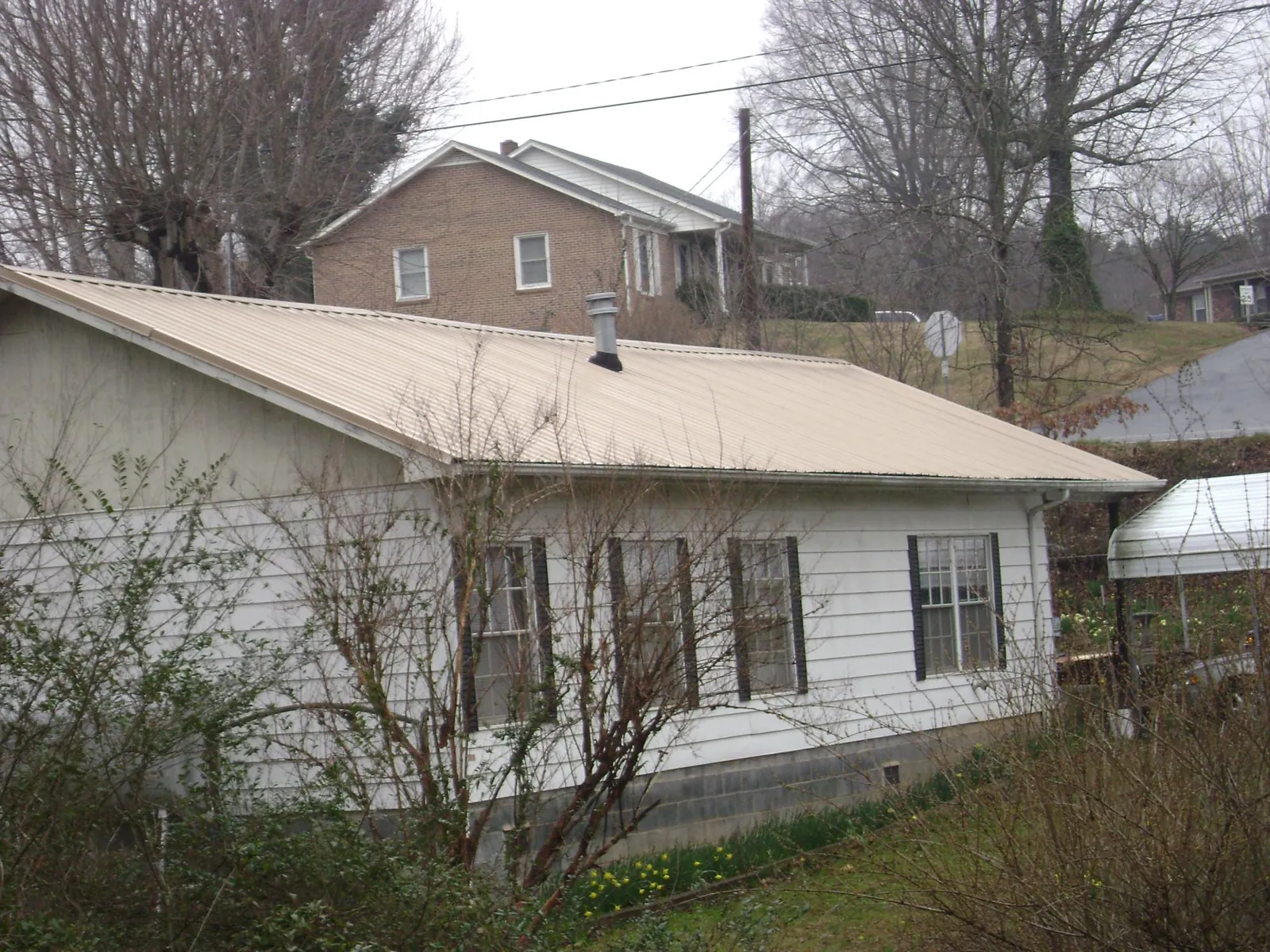 Tan metal roof on a white sided house set into a hillside — Commercial Roofing by Roofing Brothers in Genoa